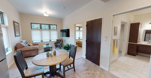 A cozy living space featuring a dining area with a round table and chairs, a television mounted on the wall, and natural light streaming through the windows.