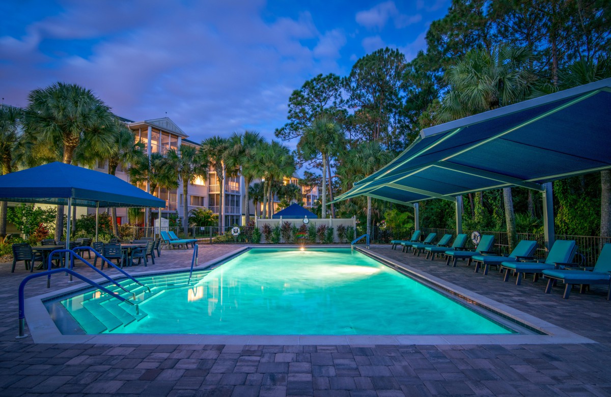 A serene resort swimming pool area illuminated at dusk, surrounded by trees and lounge chairs.