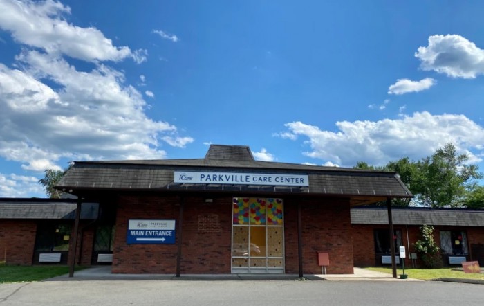 A brick building under a blue sky with scattered clouds, featuring a prominent entrance and signage.