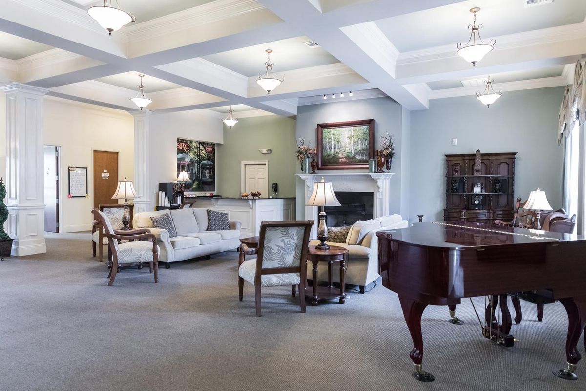 A spacious and elegantly decorated living room featuring a grand piano, comfortable sofas, and a cozy fireplace.