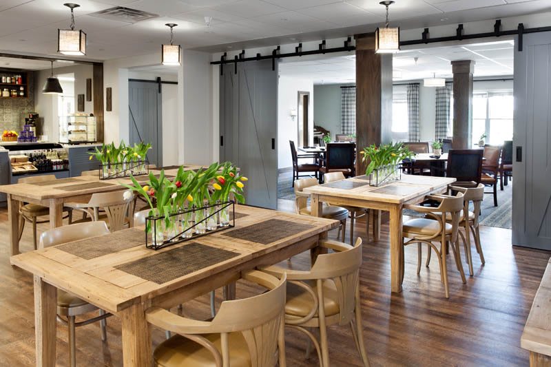 A modern dining area with wooden tables and chairs, decorated with green plants.