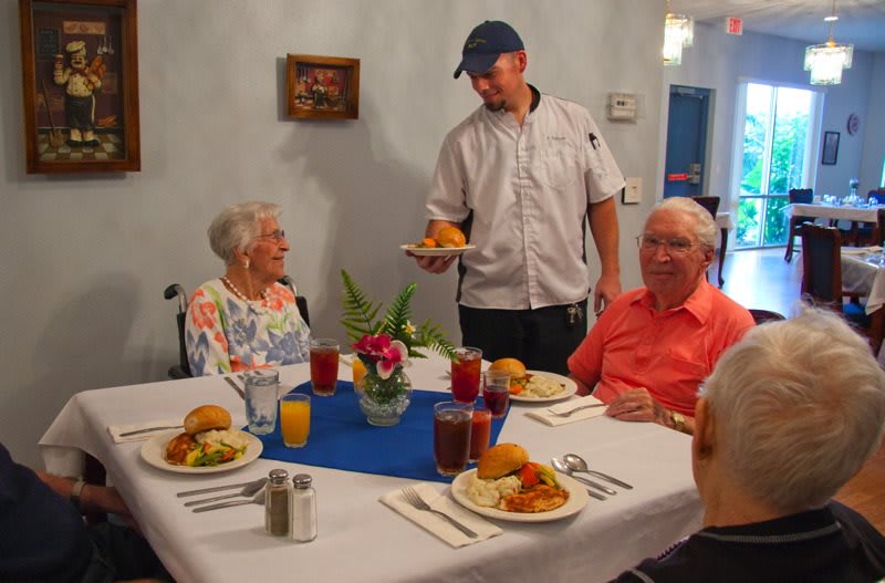 A waiter serves a meal to elderly patrons at a restaurant table.