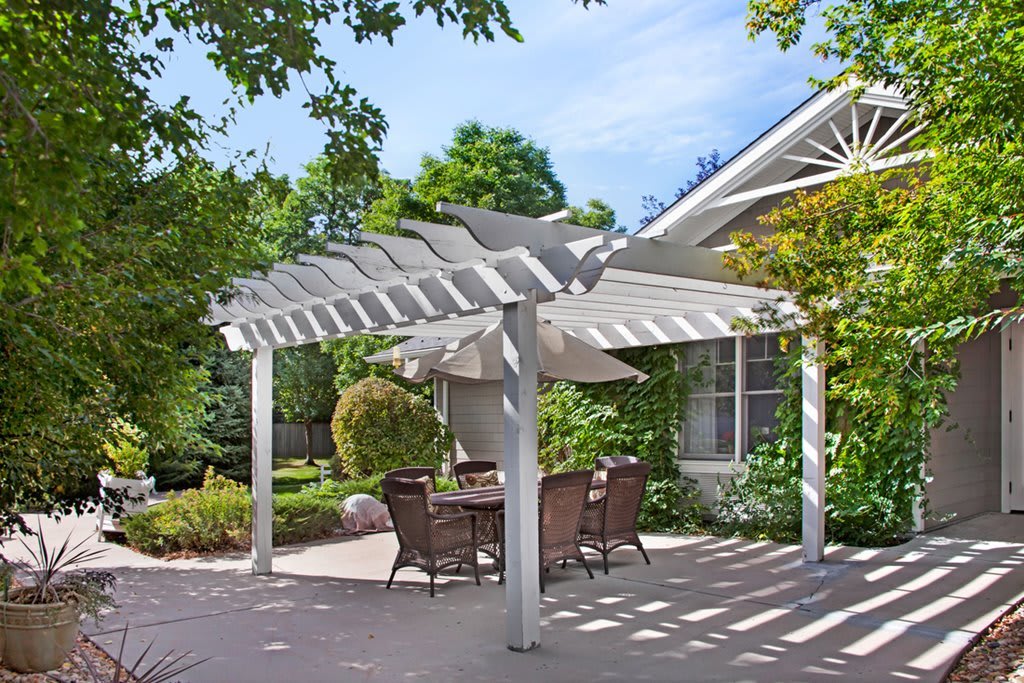 A white pergola providing shade over an outdoor dining area in a sunny backyard.
