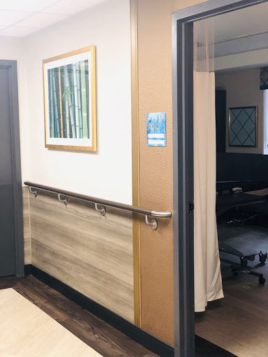 A view of a hallway leading to an office space, featuring a decorative artwork and handrails.