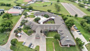 Aerial view of a large building complex surrounded by green fields and parking areas.