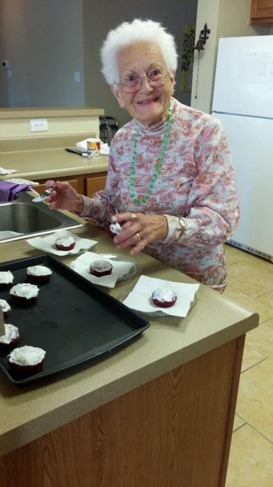 An elderly woman is frosting cupcakes in a kitchen.