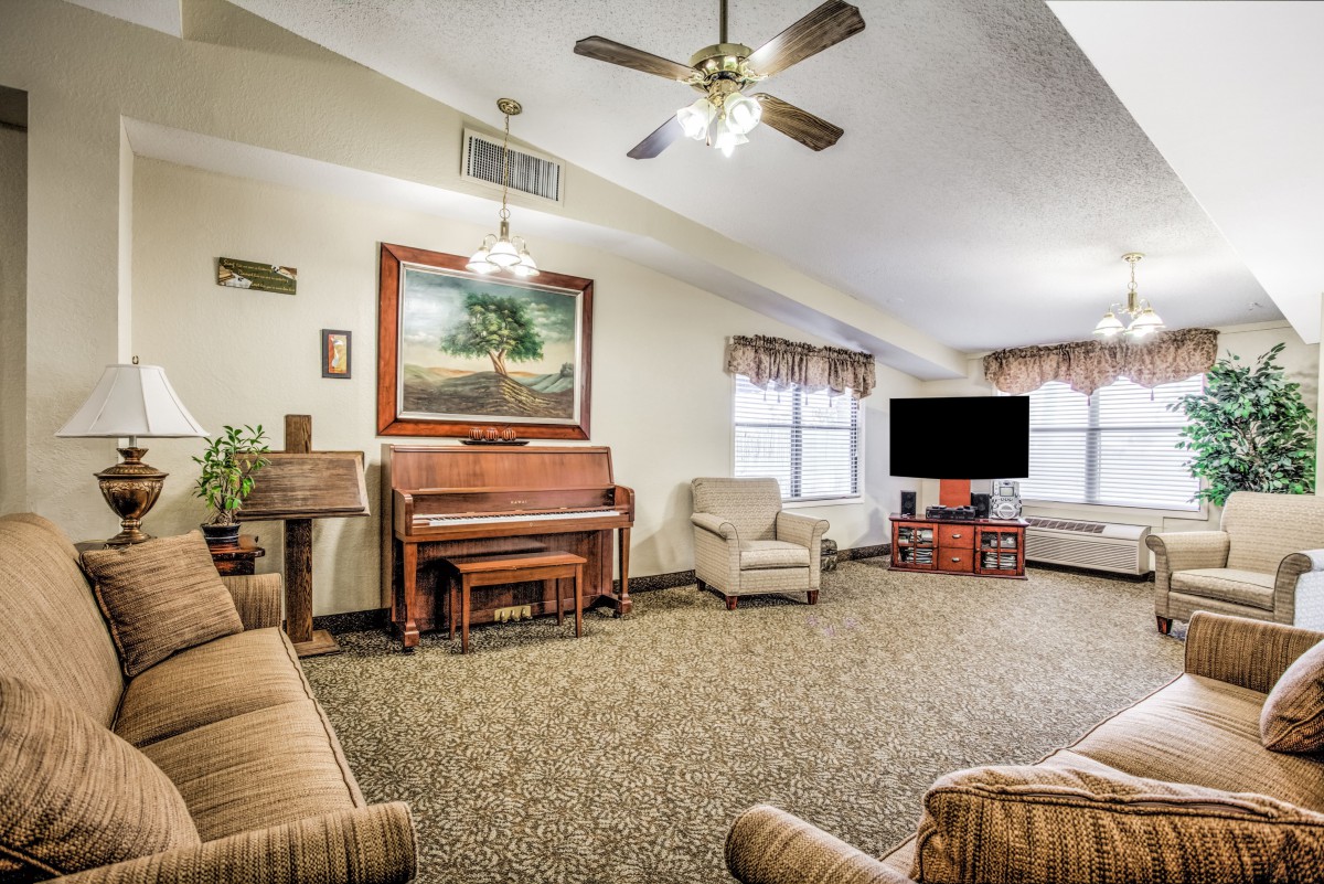 A cozy living room featuring a piano, ample seating, and a large television.