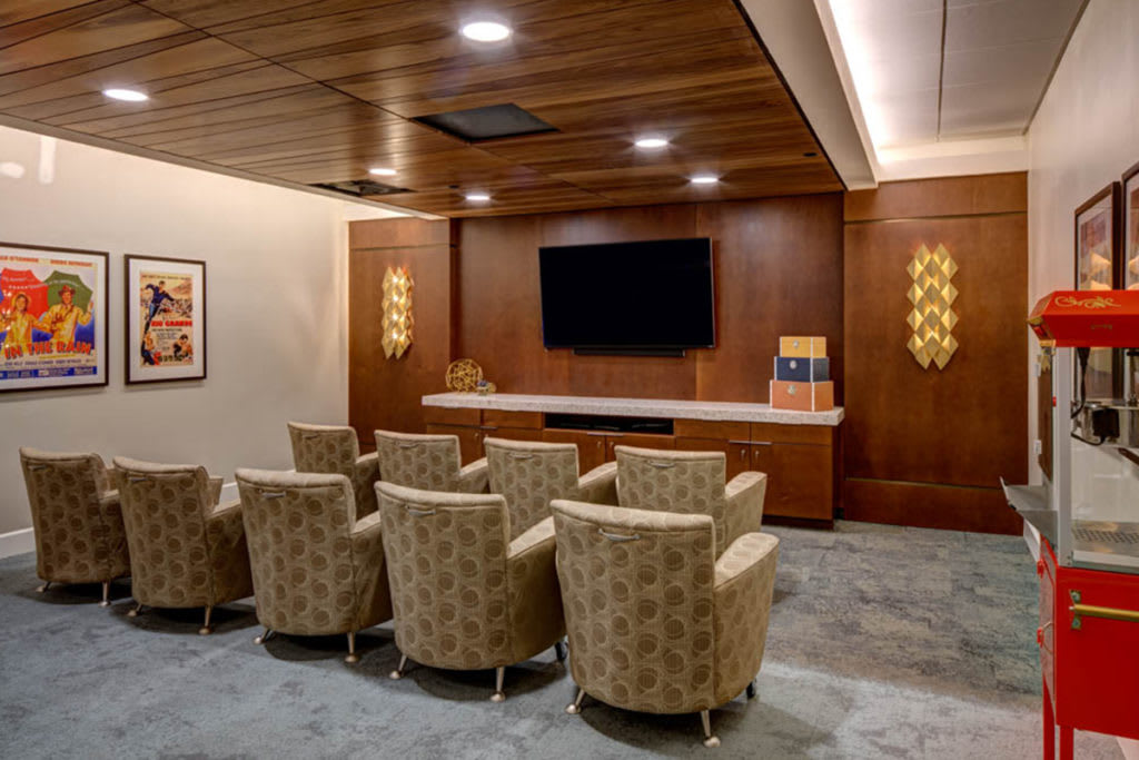 A cozy home theater room with plush seating and a wall-mounted television, featuring elegant wood paneling and soft lighting.