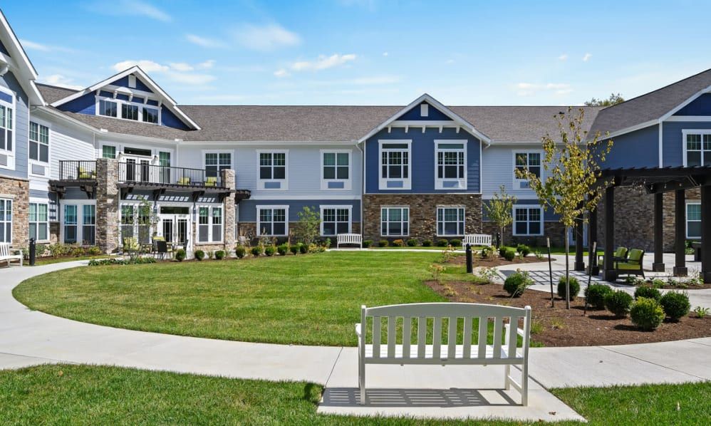 A two-story residential building with a well-maintained lawn and a white bench in the foreground on a sunny day.
