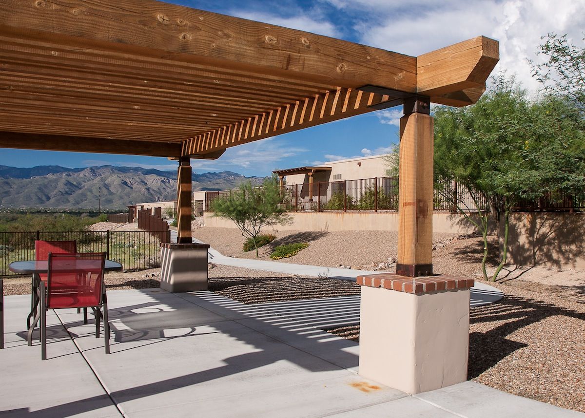 A wooden pergola providing shade in a desert backyard setting with patio furniture.