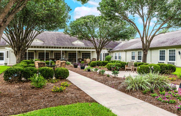 A beautifully landscaped garden with a pathway leading to a house surrounded by lush greenery and trees.