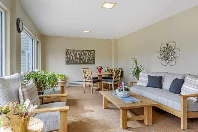 A cozy living room with natural lighting, featuring wooden furniture and indoor plants.