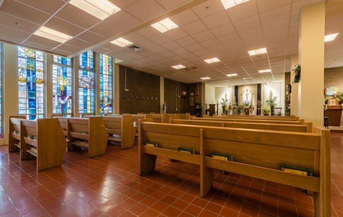 Interior of a church featuring rows of pews and stained glass windows.