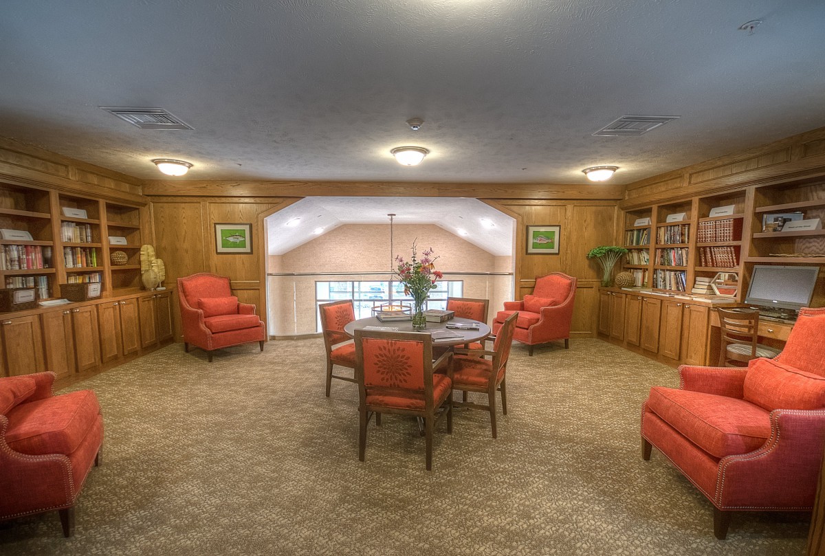 A cozy reading room with plush armchairs, a central table, and bookshelves lining the walls.