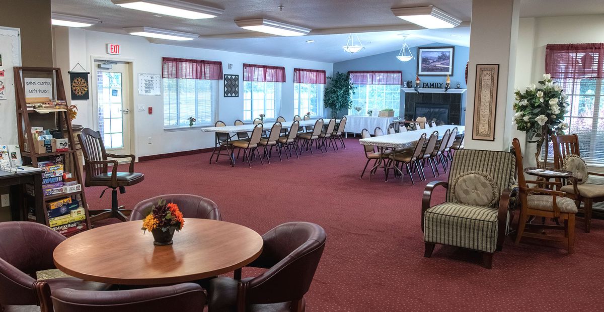 A spacious dining area with several tables and chairs, featuring large windows and a red carpet.