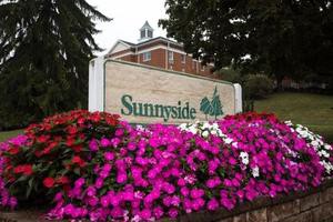 A vibrant display of flowers in front of a sign for Sunnyside, with a building in the background.