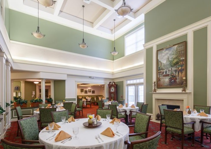 A spacious and elegantly decorated dining room with neatly arranged tables and chairs, featuring a high ceiling and soft lighting.