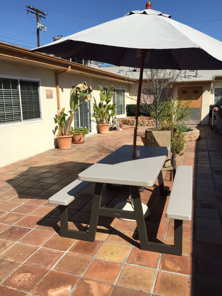 A sunny patio with a picnic table and umbrella surrounded by potted plants.