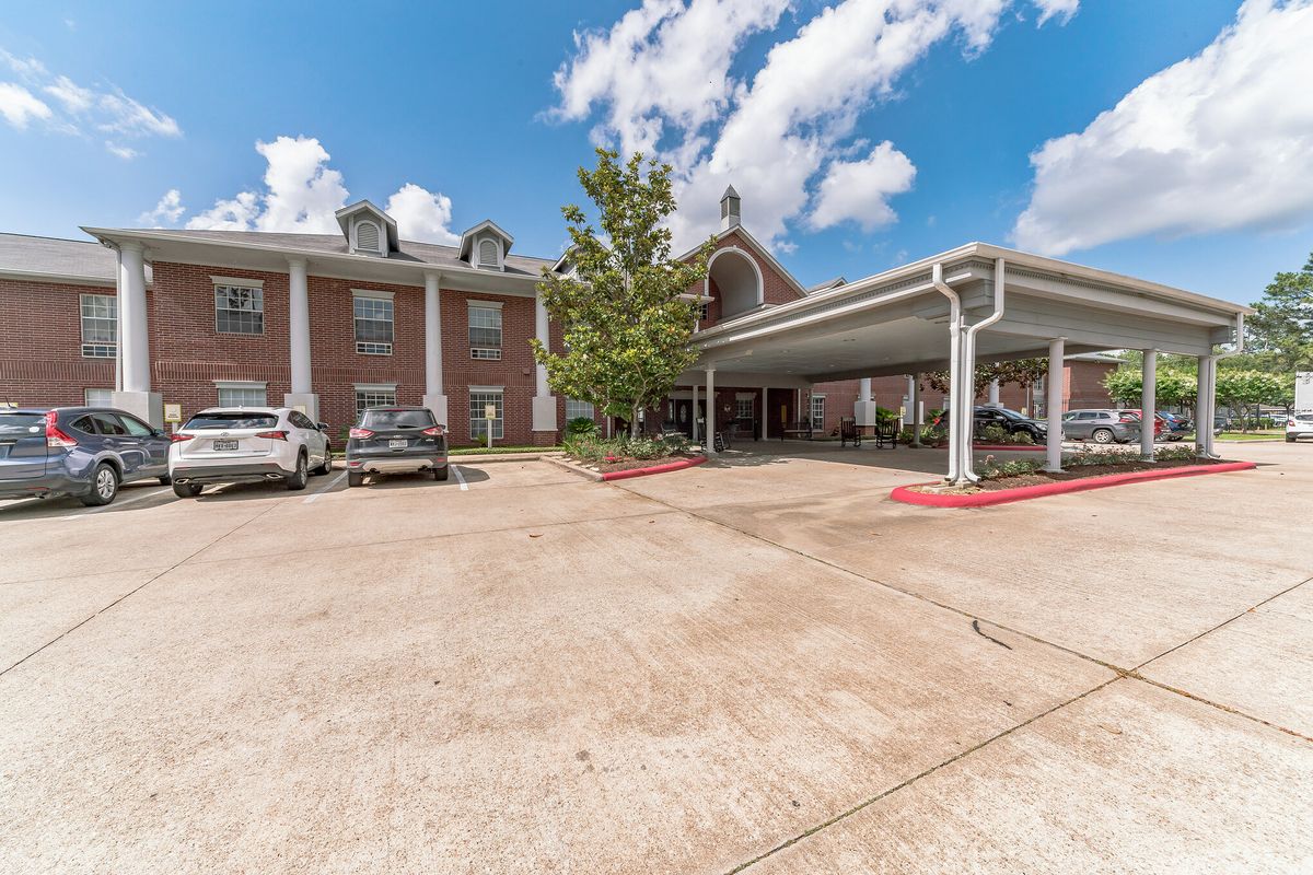 A brick building with a parking lot and several cars parked under a partly cloudy sky.