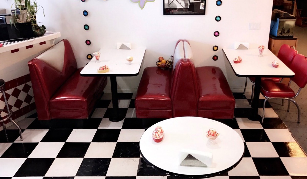 A cozy retro diner with red booths and a classic black-and-white checkerboard floor.
