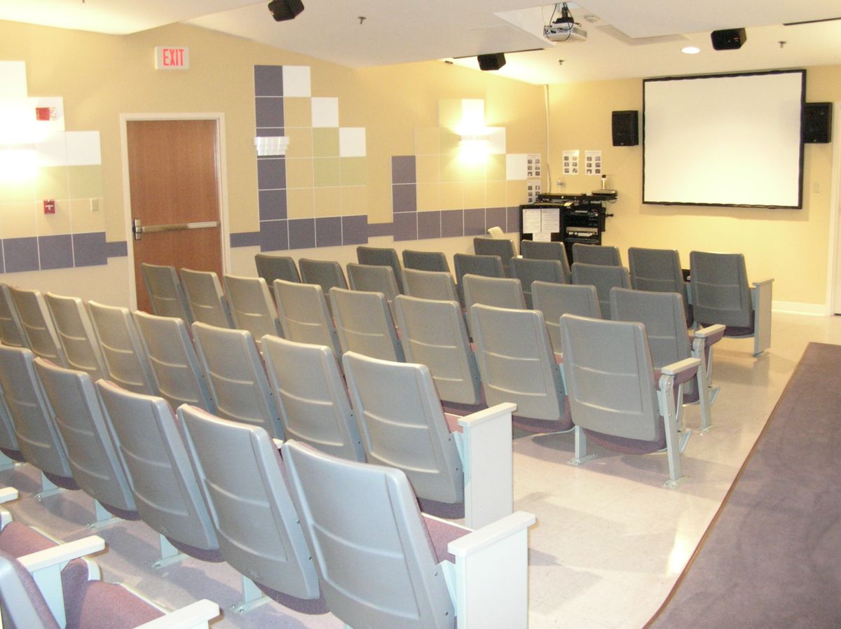 An empty auditorium with rows of chairs facing a projector screen.