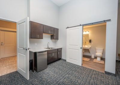 A modern office space featuring a kitchenette with cabinets and an adjacent bathroom.