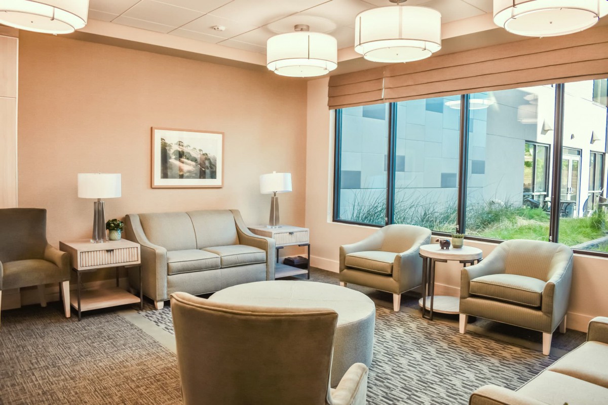 A modern waiting room with comfortable seating, soft lighting, and large windows.
