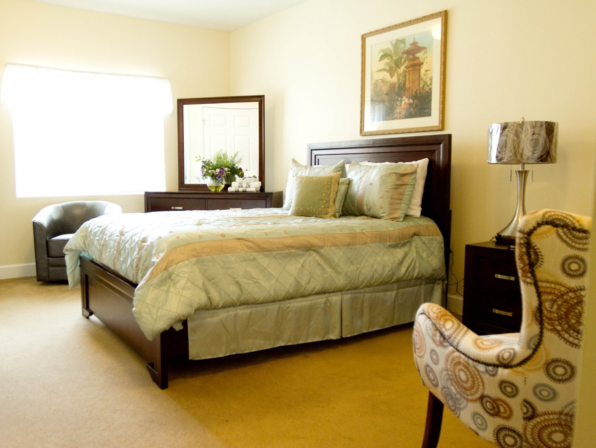 A cozy bedroom with a neatly made bed, wooden furniture, and soft lighting.