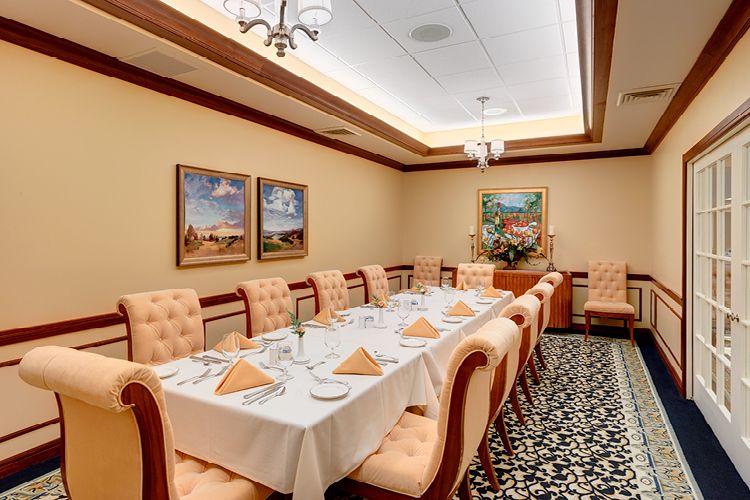 An elegant dining room with a long table set for guests, complete with upholstered chairs and decorative paintings on the walls.