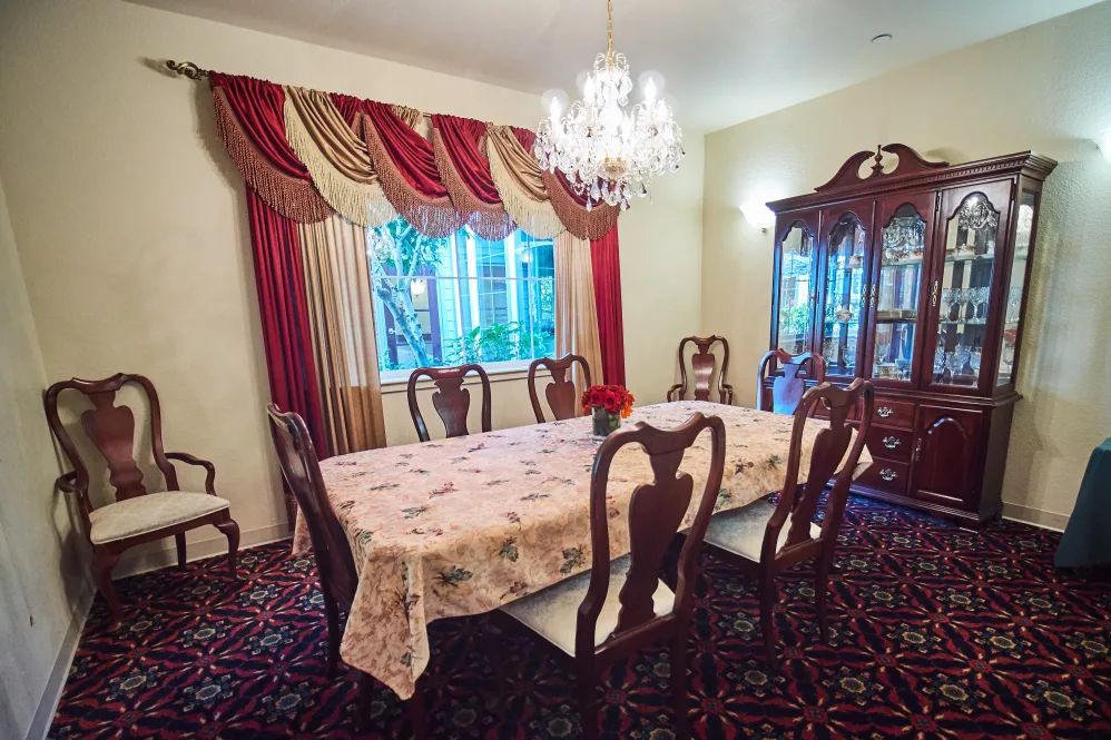 A formal dining room with elegant furnishings, featuring a chandelier and richly draped curtains.