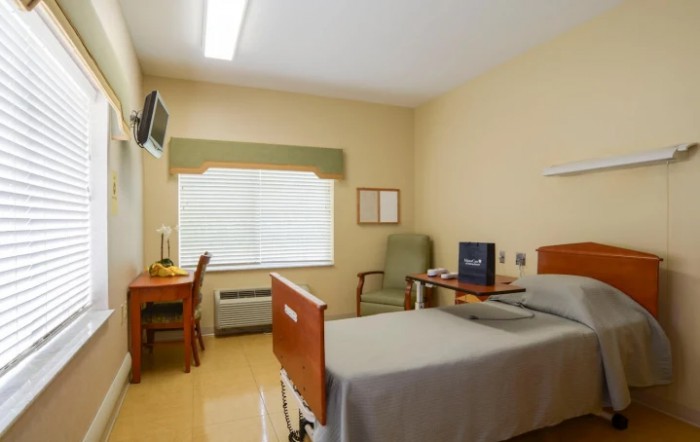 A clean and organized hospital room with a bed, desk, chair, and television.