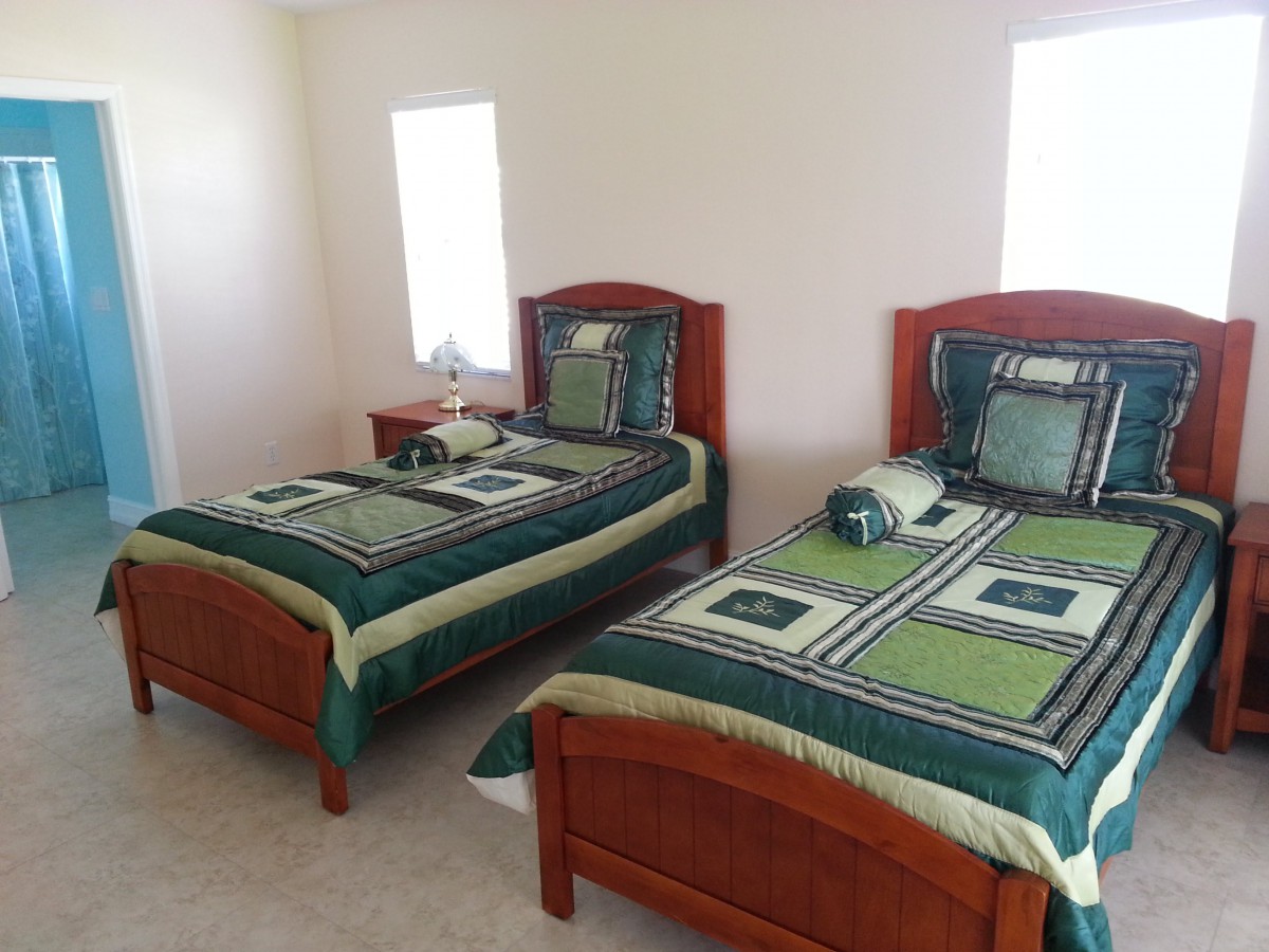 A bedroom featuring two twin beds with green and black bedding, accented by a small lamp on a bedside table.