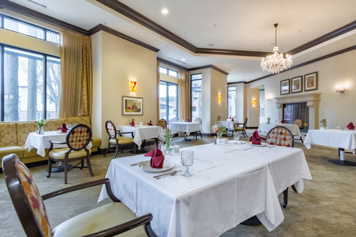 An elegant restaurant dining room with beautifully set tables, ornate chairs, and a chandelier.