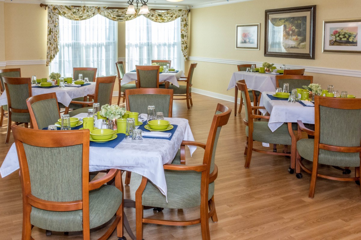 A well-decorated dining room with multiple tables and chairs, featuring neatly arranged table settings and a bright wood floor.