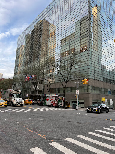 A bustling street scene in New York City featuring a modern glass building and various vehicles.