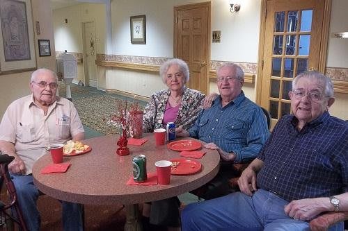 A group of senior citizens sitting at a table with snacks and drinks, enjoying a social gathering indoors.