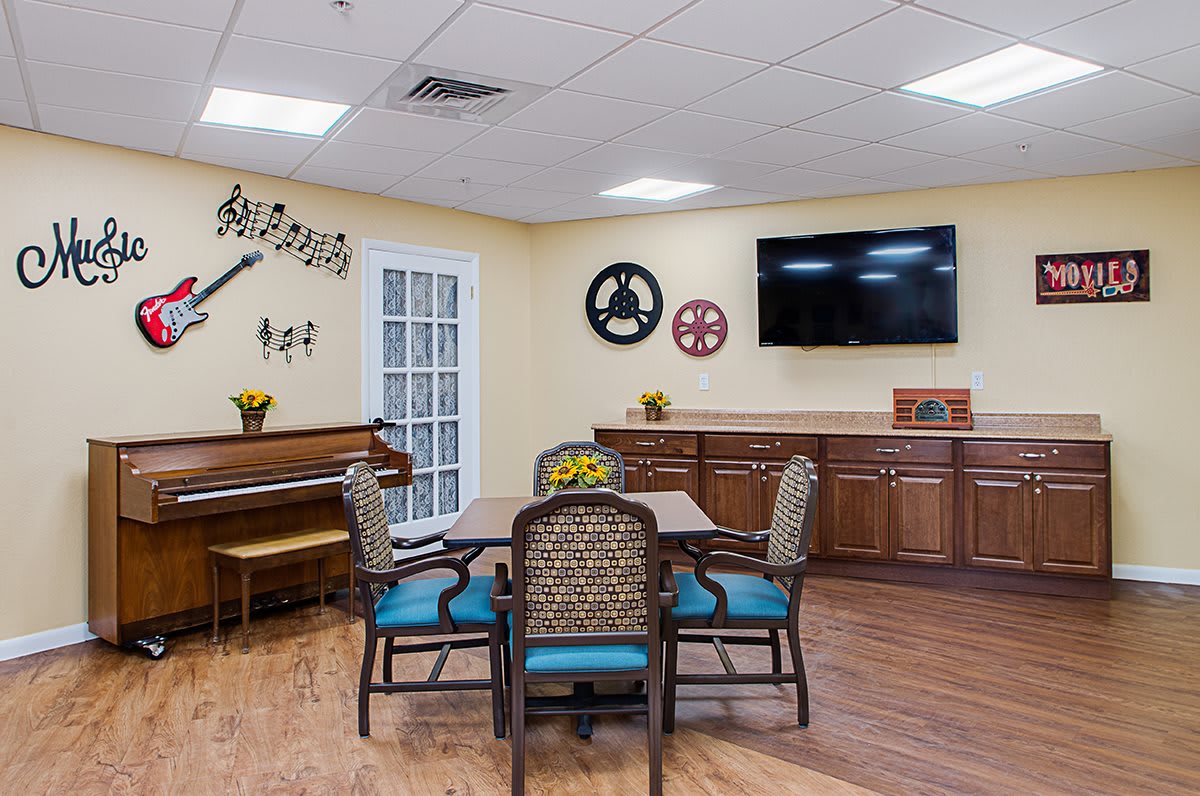 A cozy dining and recreation room featuring a piano, dining table with chairs, wall decorations, and a mounted TV.