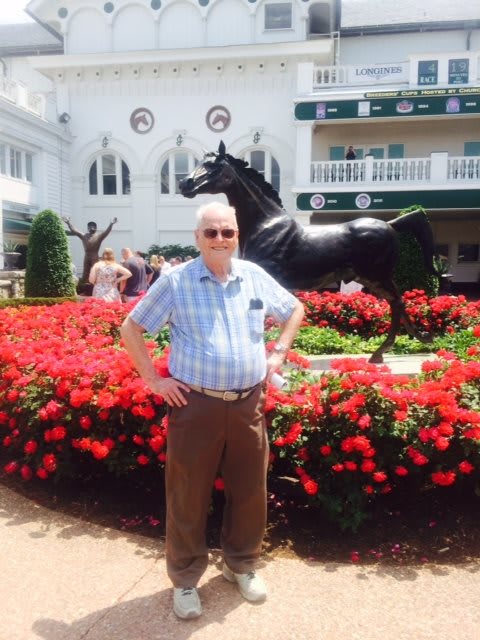 A man stands in front of a horse statue surrounded by flowers.