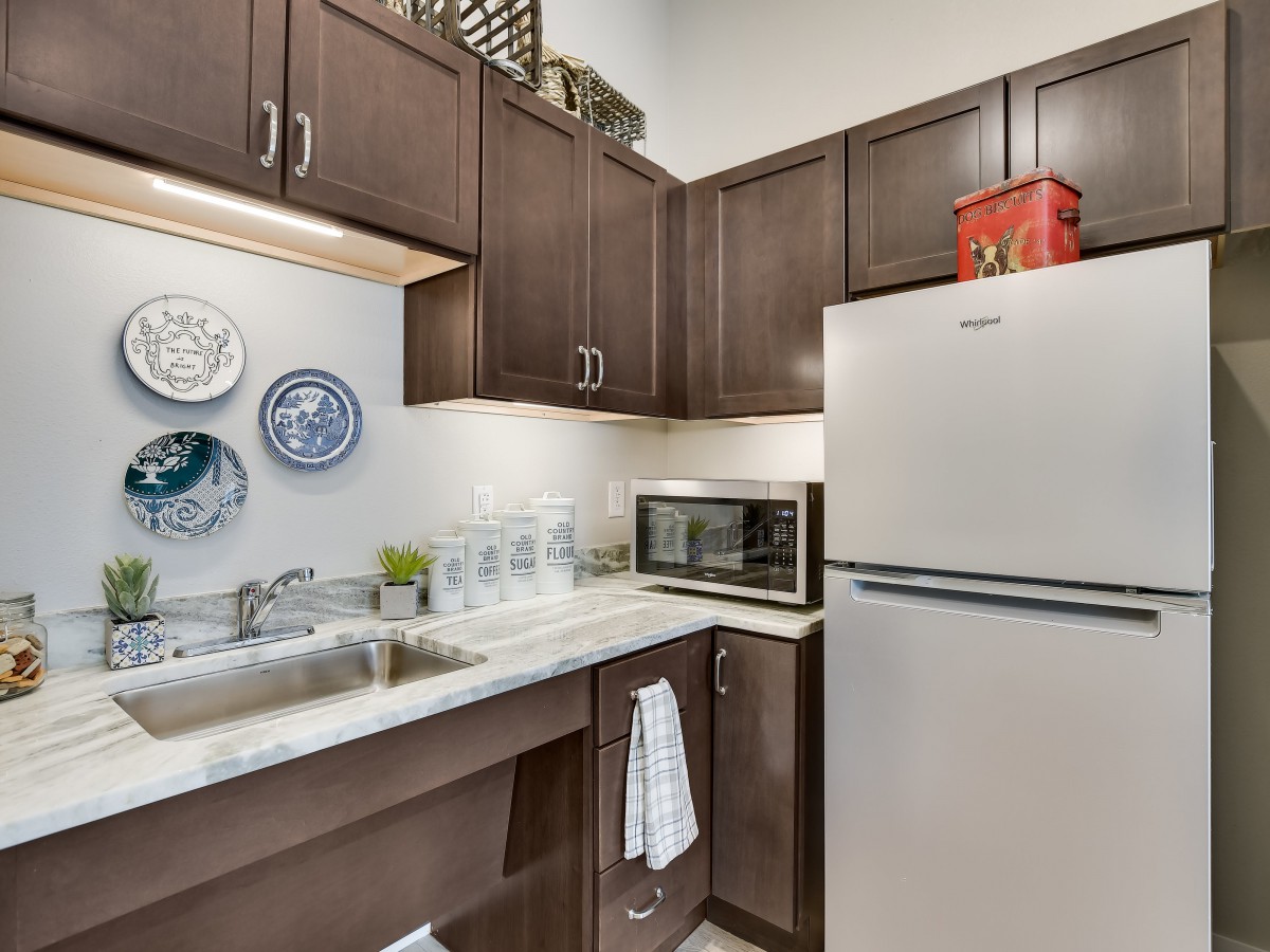 A modern kitchen with dark wooden cabinets, a stainless steel refrigerator, and a microwave on the countertop.
