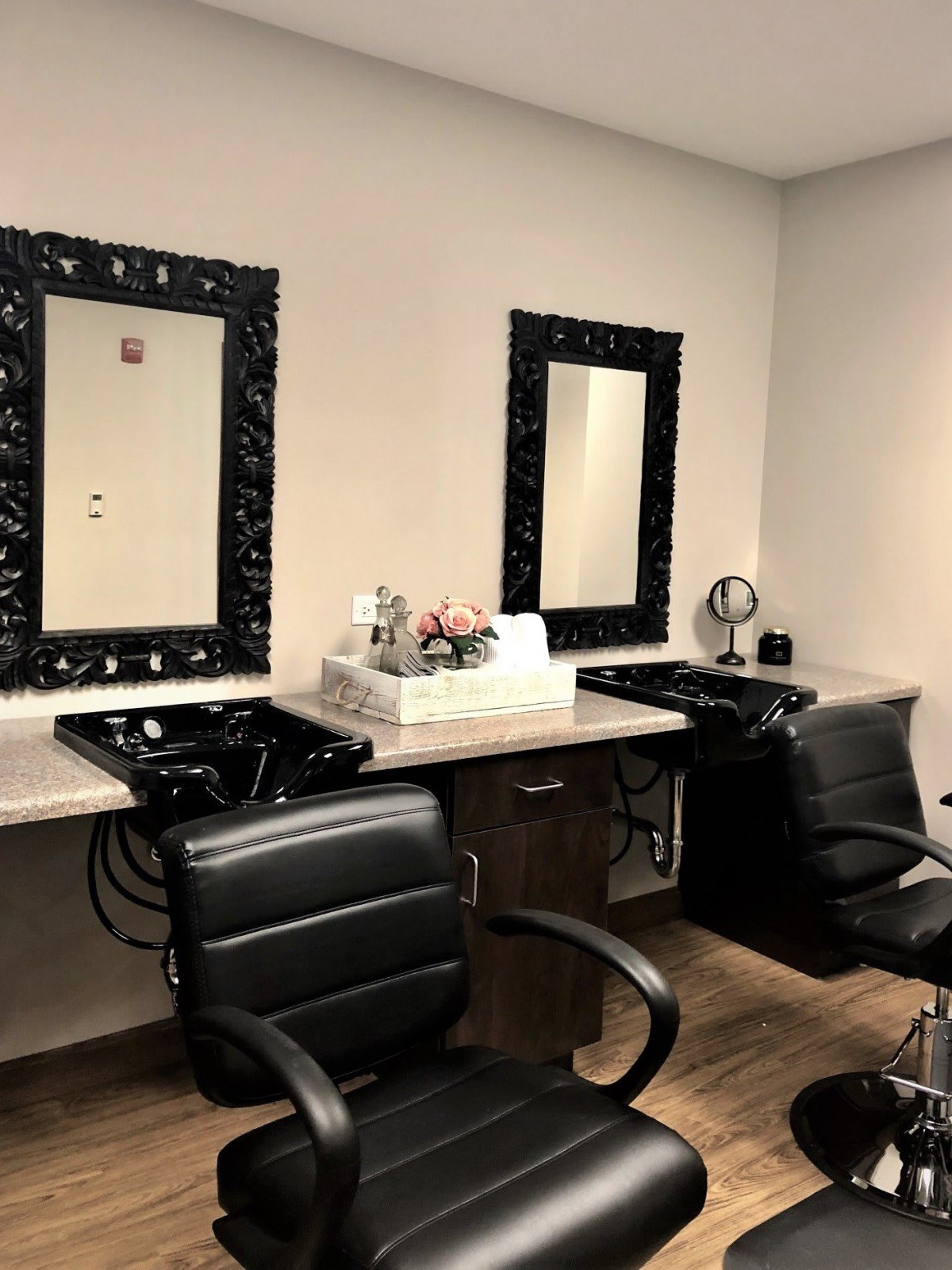 A stylish and modern salon setup with two black chairs and mirrors.