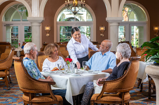 A group of elderly guests enjoying a meal at a beautifully set table, with attentive service from the waitstaff.