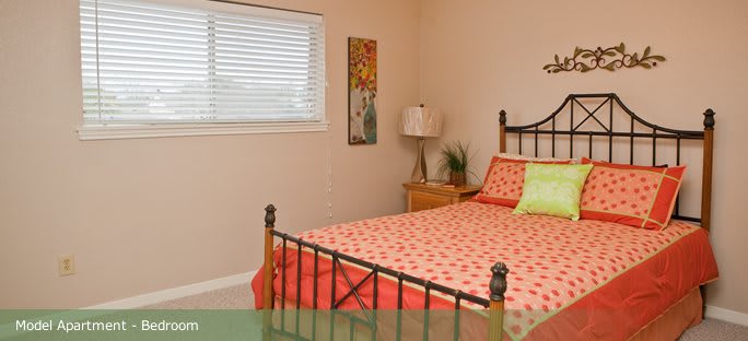 A cozy bedroom featuring a metal bed frame with colorful bedding, a nightstand with a lamp, and decorative wall art.