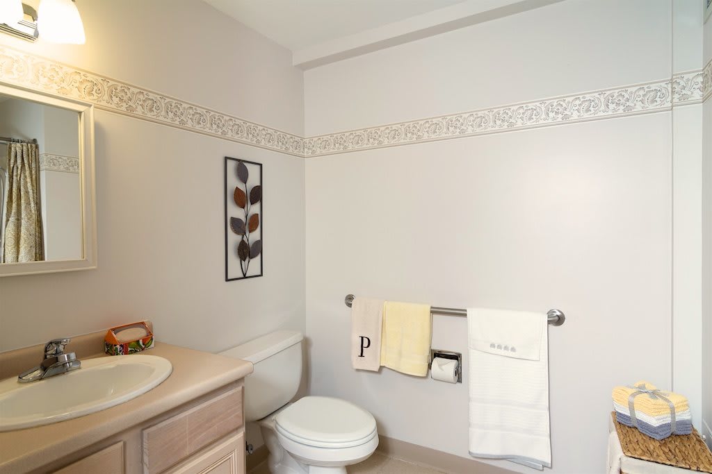A neatly arranged bathroom featuring a toilet, sink, and towels with decorative wall art and a tile border.