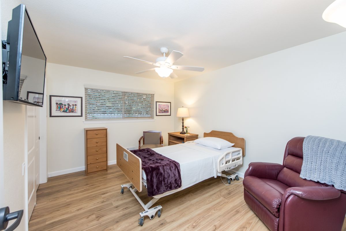 A well-lit room with a hospital bed, recliner, and wooden flooring.