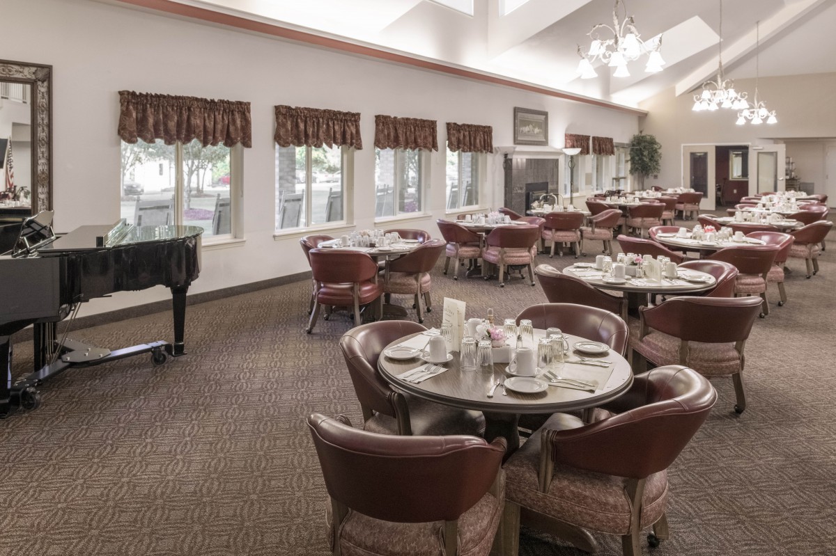 A spacious dining room with neatly arranged tables and chairs, featuring a piano in the corner.