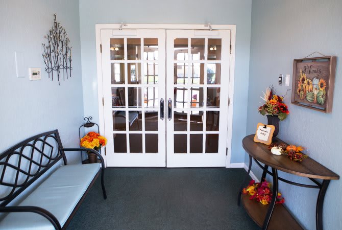 A cozy entrance with double French doors, decorated with autumn-themed items and seating.