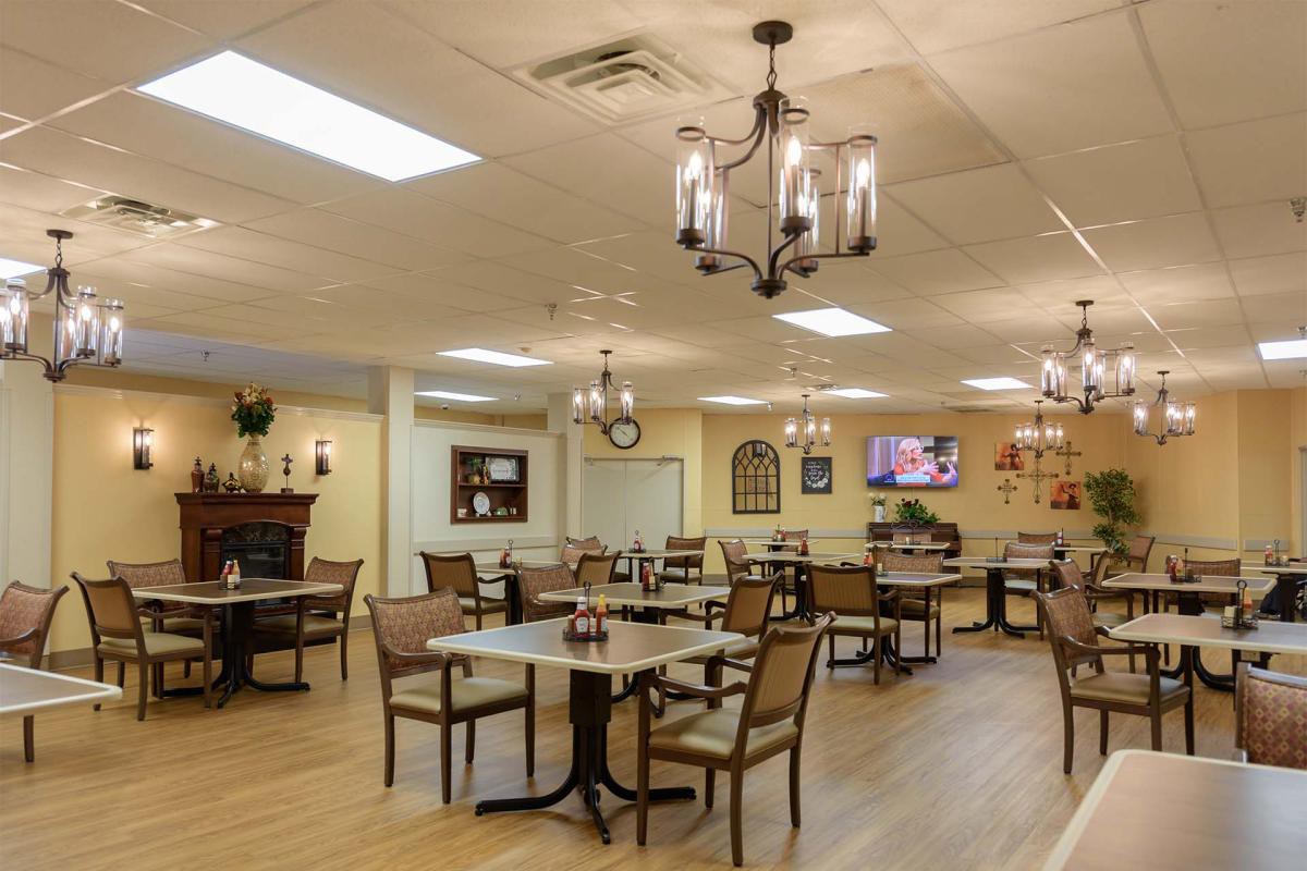 A cozy dining area with neatly arranged tables and chairs, elegant lighting fixtures, and a television mounted on the wall.