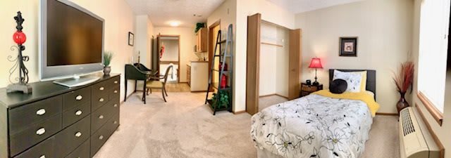 A cozy apartment interior featuring a bedroom with an open closet, a ladder shelf, and a small kitchenette.