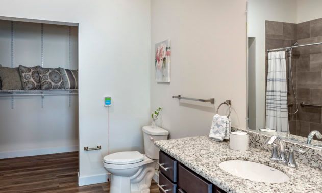 A modern bathroom with a granite countertop, sink, toilet, and towel rack.