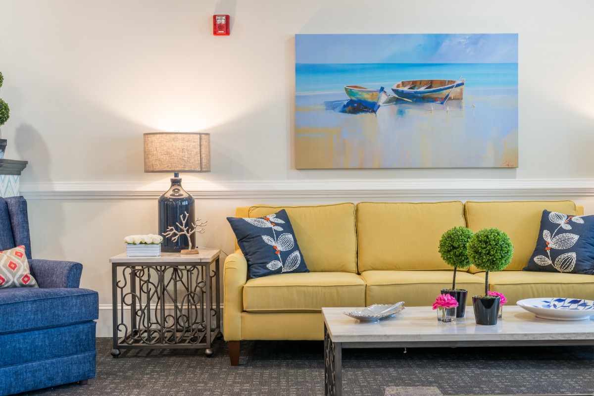 A cozy living room featuring a yellow sofa, beach-themed artwork, and elegant decor.